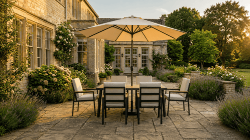 A centre-pole garden parasol shading a dining set on a stone patio at golden hour
