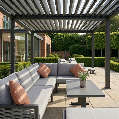 Outdoor patio with gray sectional sofa, orange cushions, and a small table under a pergola.