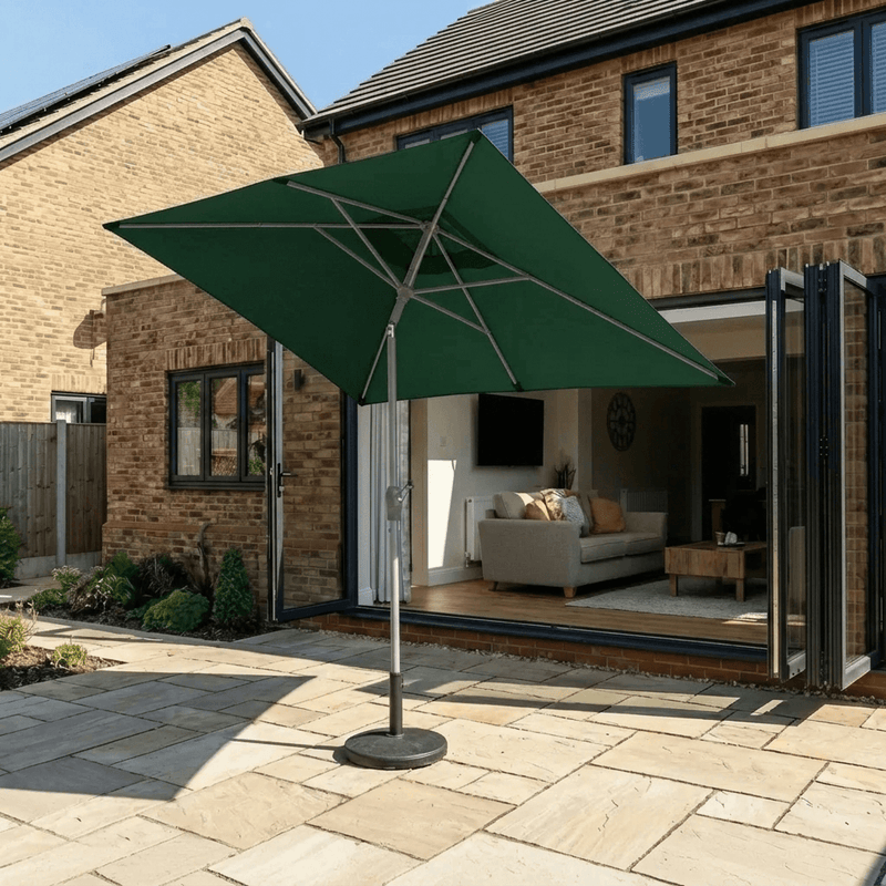 Halo 3m x 2m rectangular centre pole parasol in green, canopy tilted to angle the shade across a stone patio