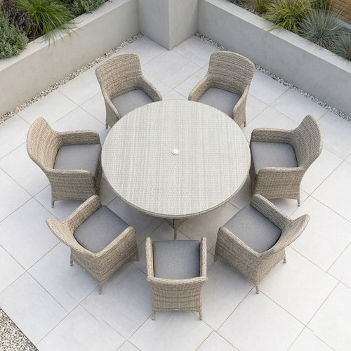 Round outdoor dining set with a woven light beige table and six matching armchairs with gray cushions, arranged on a tiled patio.