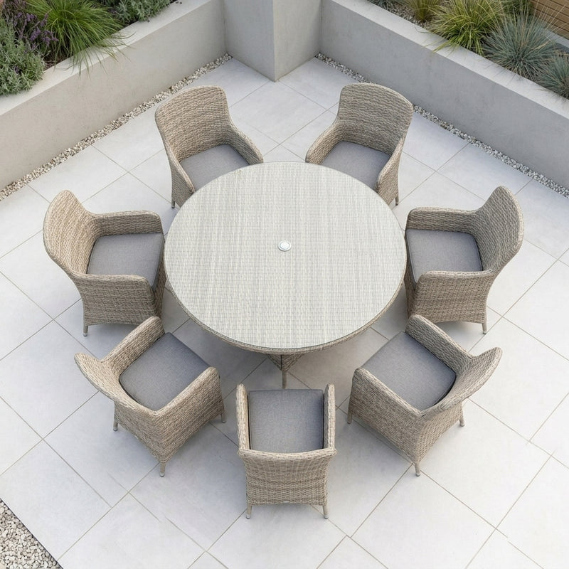Round outdoor dining set with a woven light beige table and six matching armchairs with gray cushions, arranged on a tiled patio.