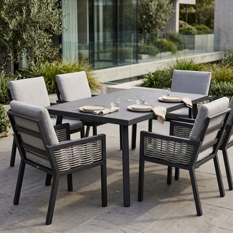 A 7-piece outdoor dining set featuring a rectangular dark gray table and six matching armchairs with light gray cushions, set on a stone patio in a modern garden environment.