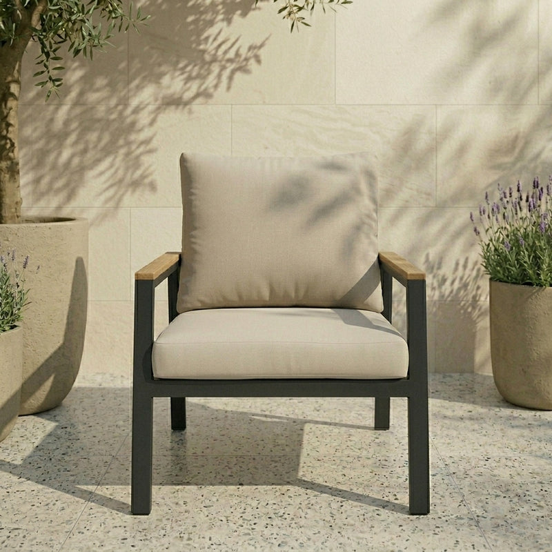 Beige cushioned chair with wooden armrests in an outdoor setting with plants and stone wall.