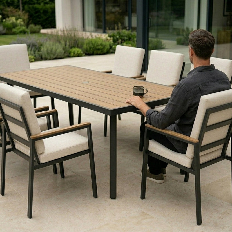 Man sitting at a wooden outdoor dining table with white chairs in a modern patio setting.