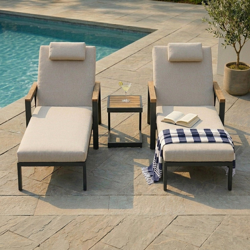 Two outdoor lounge chairs with cushions by a poolside, featuring a small table and a blanket.