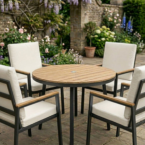 Outdoor patio set with round wooden table and four chairs with white cushions in a garden setting.